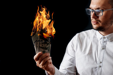 A man holds burning money in his hands, burning US dollars. The concept of inflation, a decrease in...