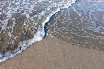 A soft foam wave rushes to the sandy beach.