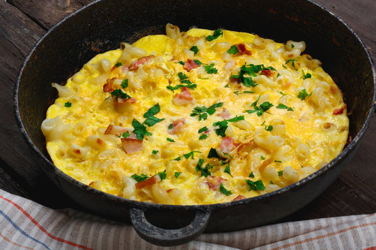 Traditional rustic omelette with bacon, pasta and greens