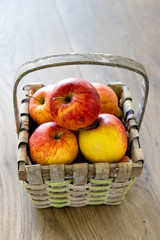 A straw basket full of apples lays on top of a wooden table