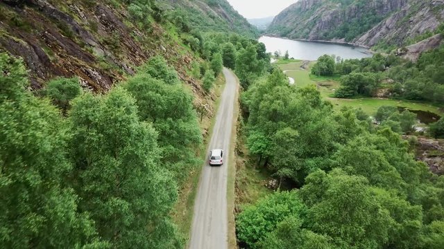 An aerial shot of a single car driving on the narrow road in the forest.