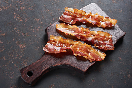 Fried bacon on wooden cutting board. Top view, isolated on black background.