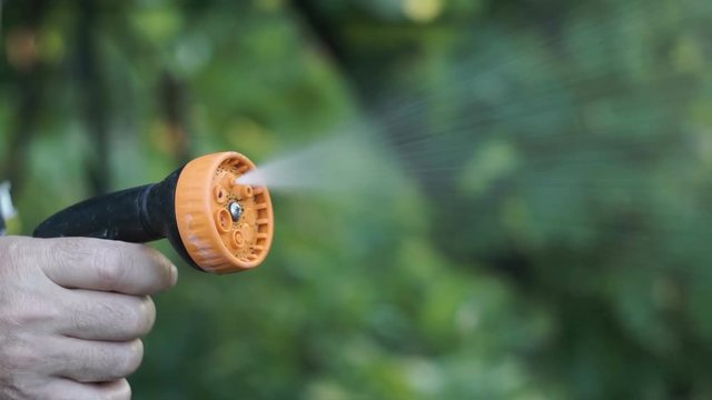 Man's hand holding water sprinkler while gardening, water spraying out of sprinkler on the grass