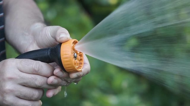 Man's hand holding water sprinkler while gardening, water spraying out of sprinkler on the grass