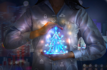 Woman holding business Christmas tree, made of neon light and surrounded by communication icons. Business background, Christmas concept. 