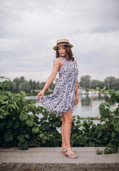 Outdoor portrait of young beautiful happy smiling woman wearing hat, blue dress near grape leaves...