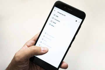 hand with smartphone, shopping list on the phone. what to buy list