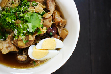 Chinese roll noodle soup with crispy pork and boil egg in white bowl on the wooden table. Asian food and street food in Thailand