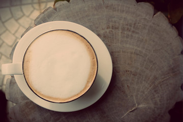 A white cup of hot coffee on wooden table in the garden of coffee shop