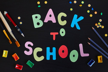 Back to school inscription made of colored letters and school supplies on the black background.