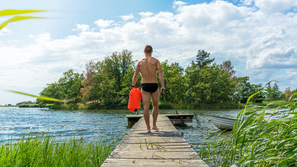 Sexy young man on a jetty with a drybag and goggles, open water swim © DZiegler