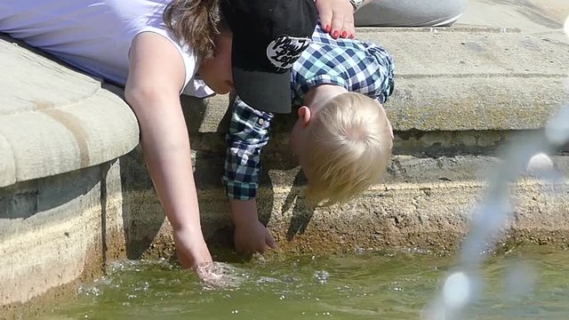 Children play with water near a fountain. Children are wetting their hands in the fountain.