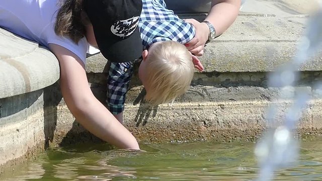 Children play with water near a fountain. Children are wetting their hands in the fountain.