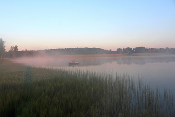 Beautiful summer nature on a pond in July. Fishermen in boats in the pre-dawn mist, in the rays of the walking sun.