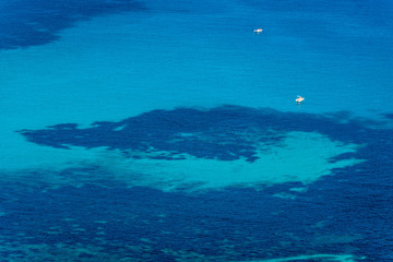 Fototapeta na wymiar Aerial view of tropical turquoise blue sea with floating boats and people. High resolution image of sailing boats anchored next to reef around the coastline. Bird's eye view, ocean from above.