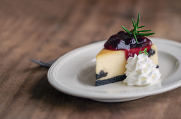 Delicious and sweet blueberry New York cheesecake on white plate served with whipped cream on wood table in side view with copy space. Homemade bakery for cafe and restaurant or birthday cake.