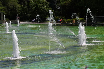 Fountain in a lake. Beautiful view of fountains in a lake with green and blue reflexion in the water. Summer in park with artificial pond and fountains. Hot Weather  concept. Summer time. People relax