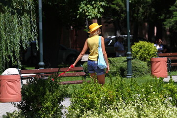 Naklejka na ściany i meble Unrecognizable woman with yellow hat and shorts rest and takes a walk in the park with a dog. Unidentified person take a walk outdoor in nature. Sport and relax concept. Good weather concept. Dog walk