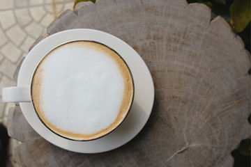 A white cup of hot coffee on wooden table in the garden of coffee shop