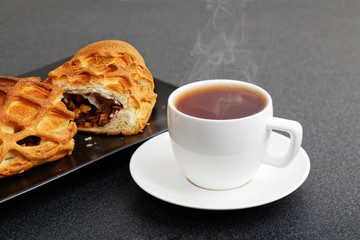 Closeup cup of tea and homemade strudel with apples, raisin and cinnamon on dark table