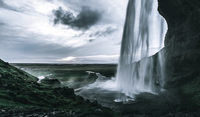 A wild natural fresh sparkling waterfall in a lonely green valley with moos covered rocks and ice cold mountain water flowing down black rocky walls on a rainy moody day in Iceland without tourists
