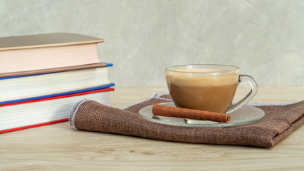 A cup of coffee and a pile of a book on a wooden table.