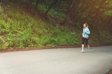 A young blonde woman running is practicing outdoors in a city mountain park in the forest. Warm rays through the branches of trees