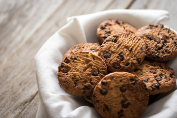 Chocolate chips cookies in a basket on wooden background, homemade sweet and dessert concept