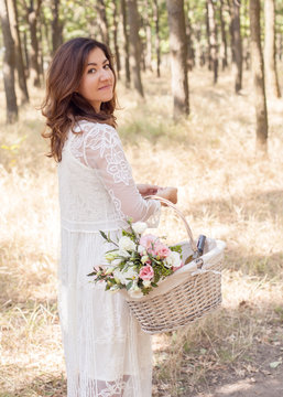 beautiful, young girl in white, lace dress with a basket and a fragrant bouquet of flowers from the eustom, roses and greens. close-up portrait of a woman of european appearance walking in the park