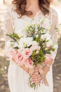 beautiful, fresh, tender bouquet of eustom, roses and greenery in the hands of a young girl on a white lace wedding dress background close-up