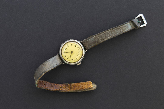 Closeup of a retro style yellow colored wristwatch with worn leather straps on black background.