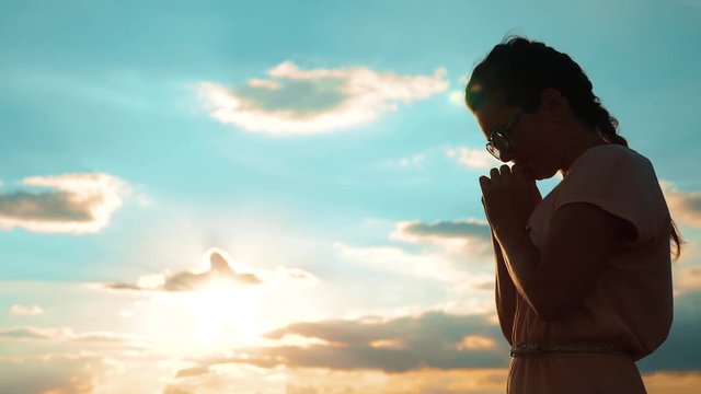 girl praying. girl folded her hands in prayer silhouette at sunset. slow motion video. Girl folded her hands in prayer pray to God. asks forgiveness for sins of repentance. believing girl. concept