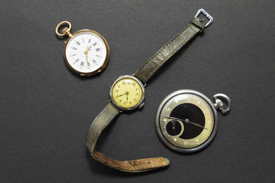Set of watches on black background with a classic gold pocket watch a black and silver pocket watch and a wristwatch with worn leather straps