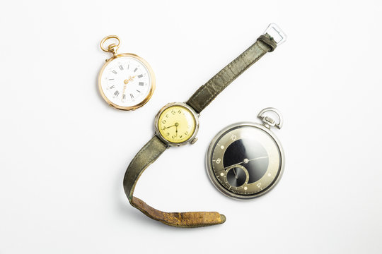 Set of watches on white background with a classic gold pocket watch a black and silver pocket watch and a wristwatch with worn leather straps