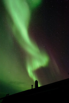 Aurora borealis above house roof and chimney