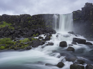 Oxararfoss waterfall in Thingvellir Iceland nature reserve with volcanic rocks and moss, falling from fissure in Mid-Atlantic Ridge, long exposure motion blur