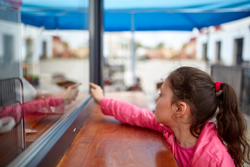 Curious little girl waiting for her burger in the street shop window.