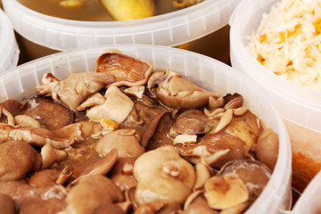 Pickled milk mushrooms and other food on a market stall. Pile of Lactarius mushrooms salted in a bucket for sale
