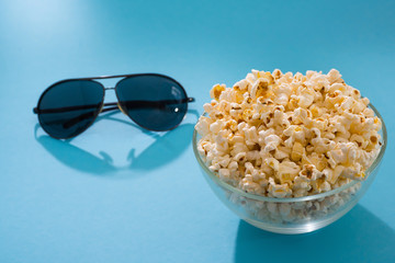 Popcorn and glasses on a blue background. Cinema background. Concept pastime, entertainment and cinema.