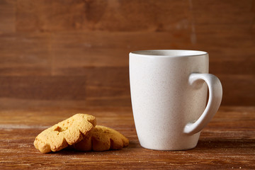 White porcelain mug of tea and sweet cookies on piece of wood over wooden background, top view, selective focus