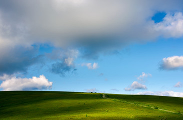 grassy hillside and gorgeous afternoon cloudscape. countryside road winds uphill in to the distance. wonderful nature background.