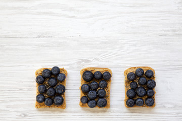 Vegetarian toasts with peanut butter, blueberries and chia seeds on a white wooden table, top view. Healthy dieting. Copy space and text area.