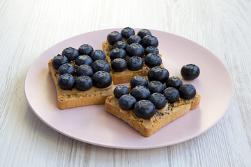 Vegetarian toasts with peanut butter, blueberries and chia seeds on a pink plate over white wooden surface, top view. Healthy eating. Side view.