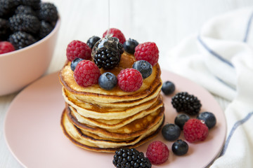 Pancakes with berries and honey on a round pink plate, side view. Close-up.