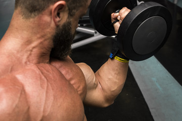 Hombre fuerte con grandes músculos entrenando con mancuernas  en el gimnasio. Ponerse en forma.