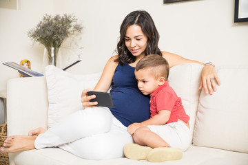 Pregnant Mother And Son Using Smartphone At Home