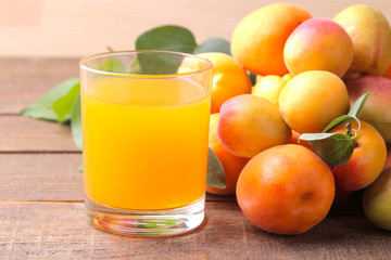 Apricot juice in a glass cup next to fresh apricots on a brown wooden background