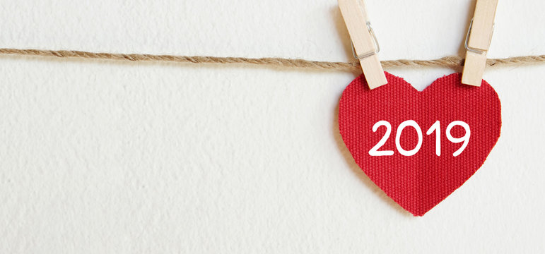 2019 new year greeting card template, Red fabric heart with 2019 word hanging on white wall background with copy space