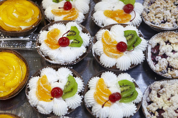 Fruit creamy cakes with canned cherry, orange and kiwi topping.