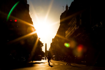 Avenue with solar backlight, people walking and obelisk of Buenos Aires in the background